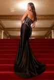 Woman in a black evening gown standing on red steps inside an elegant building.