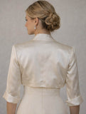 Woman wearing an ivory satin jacket over a dress against a plain background