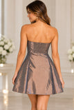 A woman shown from the back wearing a strapless metallic bronze mini dress with a flared skirt, set against a bright, softly blurred indoor background.