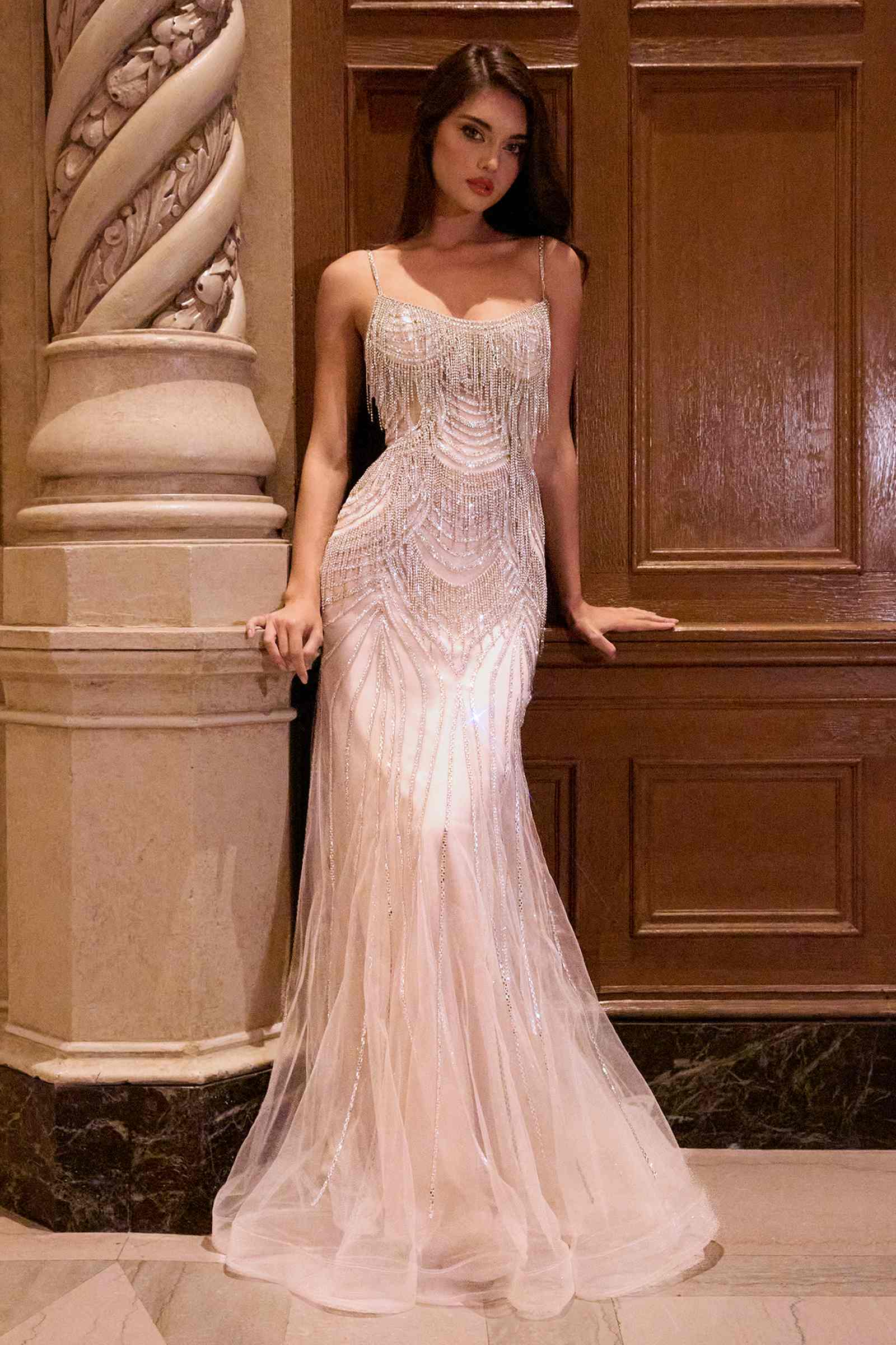Woman in a beaded evening gown standing in an elegant interior setting.